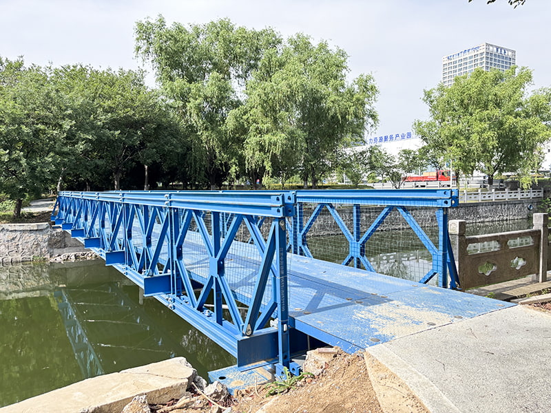 24 metrov dlhý, modro natretý antikorózny, jednoradový jednovrstvový vystužený most pre chodcov Bailey